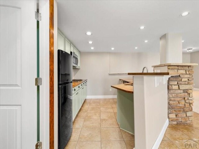 kitchen with a peninsula, white cabinetry, freestanding refrigerator, stainless steel microwave, and a kitchen bar