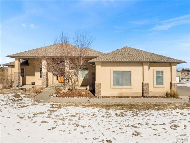 snow covered house featuring roof with shingles and stucco siding