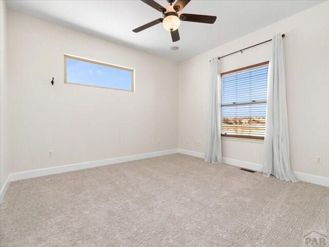 empty room featuring light carpet, ceiling fan, visible vents, and baseboards