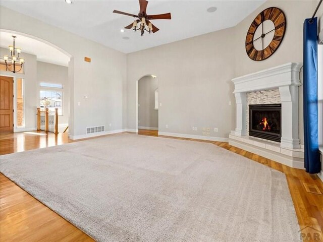 unfurnished living room with light wood-type flooring, a fireplace, visible vents, and ceiling fan with notable chandelier