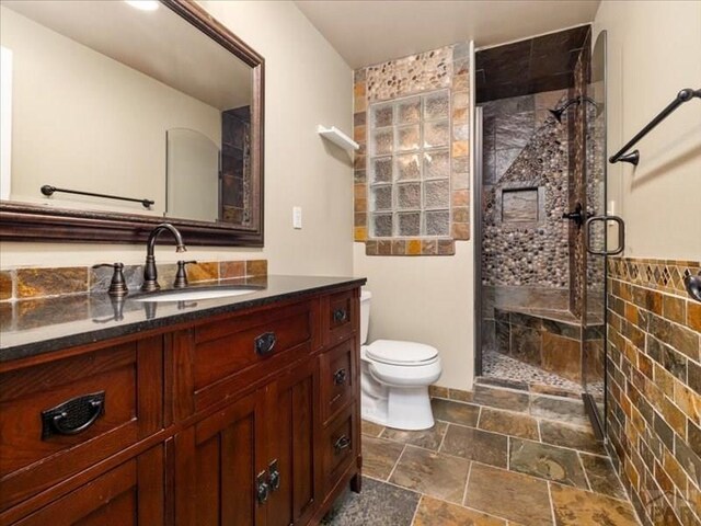 bathroom with stone tile flooring, vanity, toilet, and a shower stall