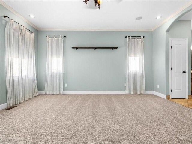 spare room featuring light carpet, baseboards, arched walkways, and crown molding