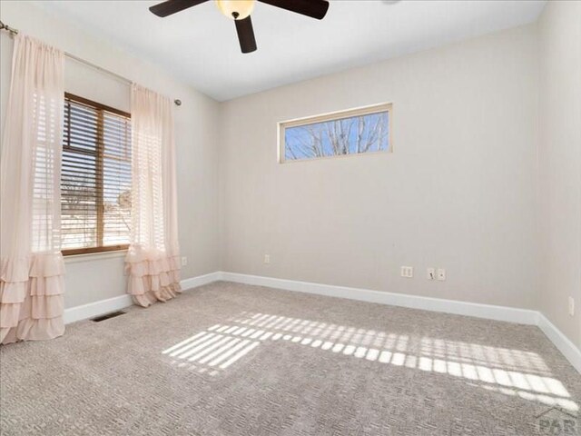 spare room with ceiling fan, light colored carpet, visible vents, and baseboards