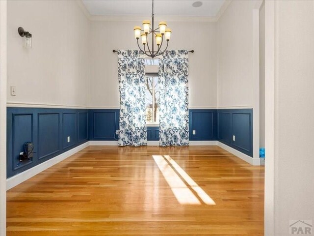 unfurnished dining area with ornamental molding, a decorative wall, wood finished floors, and a chandelier