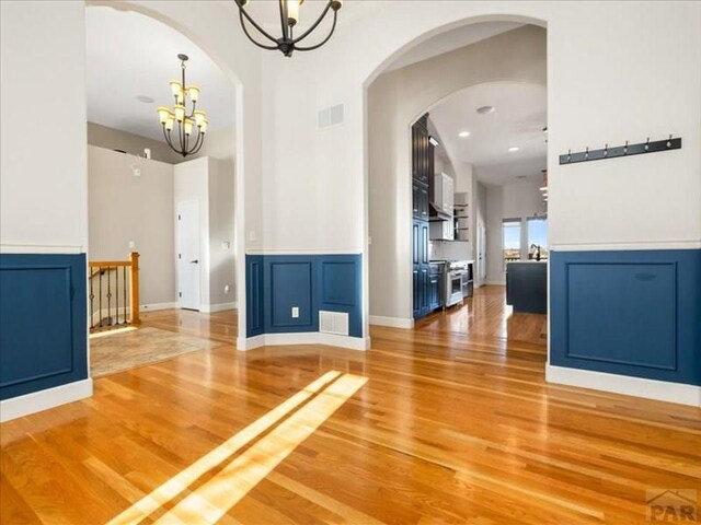 interior space with arched walkways, wood finished floors, visible vents, and an inviting chandelier