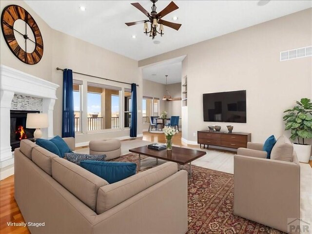 living area with visible vents, a ceiling fan, a glass covered fireplace, wood finished floors, and recessed lighting