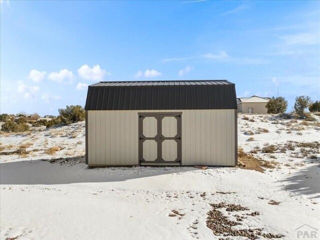 snow covered structure featuring a storage unit and an outbuilding