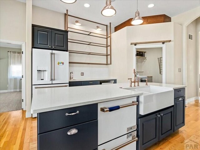 kitchen featuring pendant lighting, light countertops, a sink, an island with sink, and white appliances