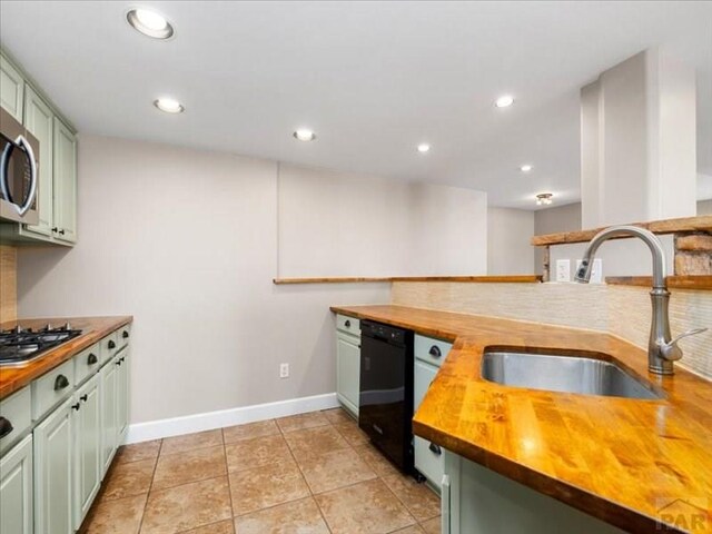 kitchen with butcher block counters, appliances with stainless steel finishes, a sink, green cabinets, and backsplash