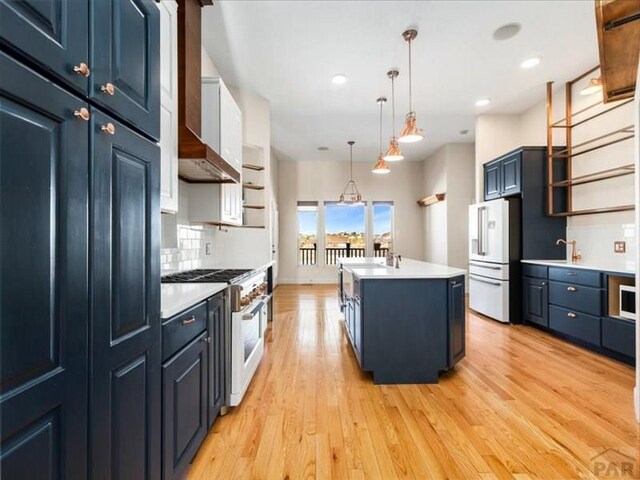 kitchen featuring premium appliances, light countertops, hanging light fixtures, open shelves, and a center island with sink