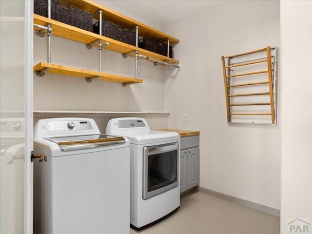 clothes washing area featuring independent washer and dryer, cabinet space, and baseboards