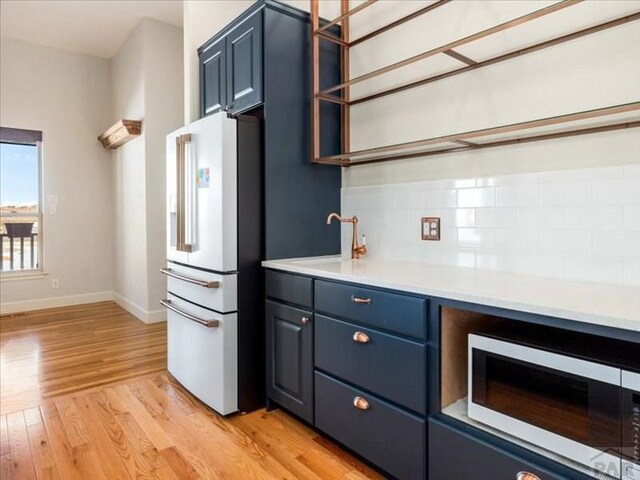 kitchen featuring high end refrigerator, light wood-style flooring, stainless steel microwave, light countertops, and a sink