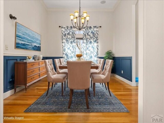 dining room with a wainscoted wall, ornamental molding, and an inviting chandelier