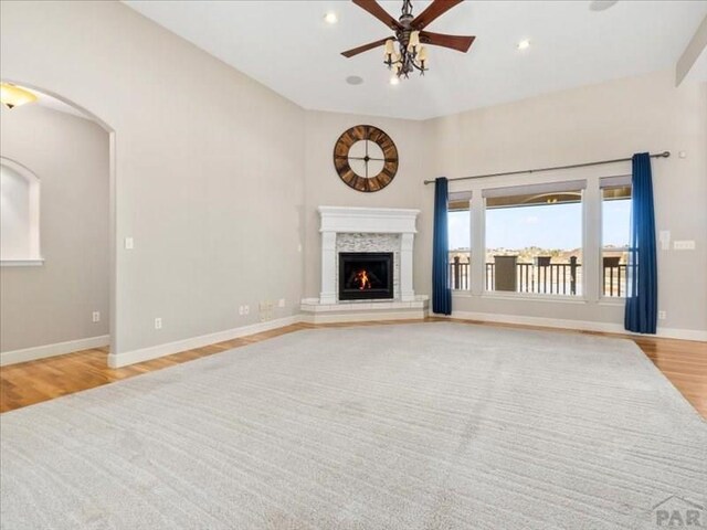 unfurnished living room featuring light wood-style flooring, recessed lighting, a ceiling fan, baseboards, and a lit fireplace