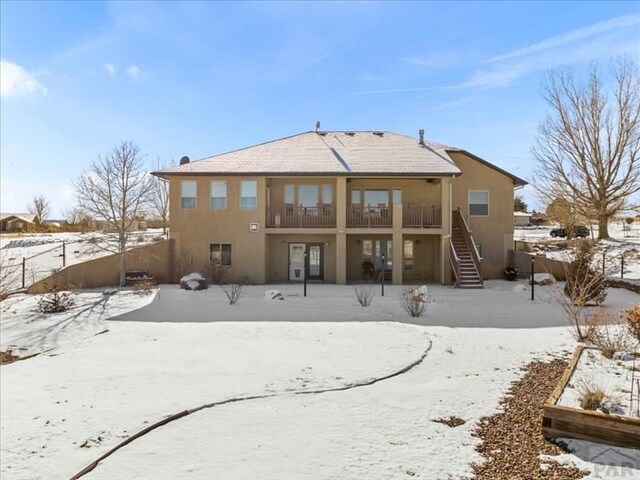 snow covered house featuring stairway and stucco siding