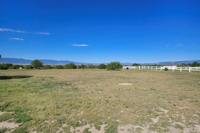 view of yard featuring a rural view, a mountain view, and fence