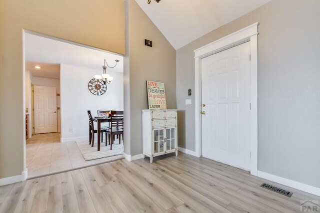 entrance foyer featuring a notable chandelier, lofted ceiling, visible vents, light wood-style floors, and baseboards