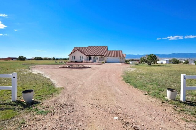 ranch-style home featuring a tile roof, dirt driveway, a mountain view, and a front yard