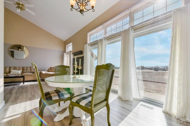 dining space featuring light wood-type flooring, an inviting chandelier, visible vents, and vaulted ceiling