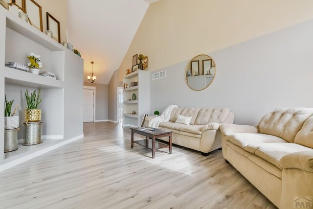 living area featuring visible vents, baseboards, light wood-style flooring, an inviting chandelier, and high vaulted ceiling