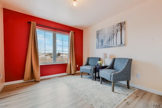 sitting room with visible vents, light wood-style flooring, and baseboards