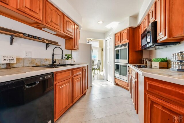 kitchen featuring brown cabinets, a sink, black appliances, and light tile patterned floors