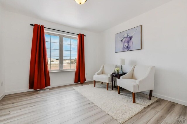 sitting room with light wood-style floors, visible vents, and baseboards