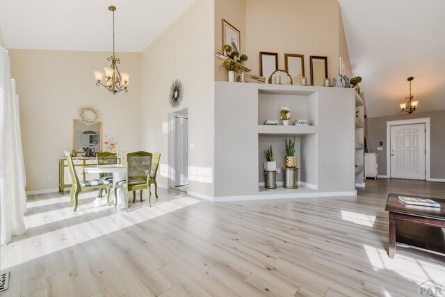 dining space with a towering ceiling, an inviting chandelier, baseboards, and light wood-style floors