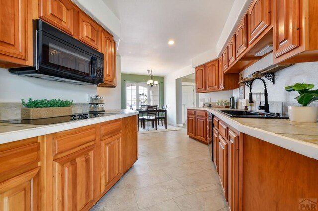 kitchen featuring brown cabinetry, hanging light fixtures, light countertops, black appliances, and a sink