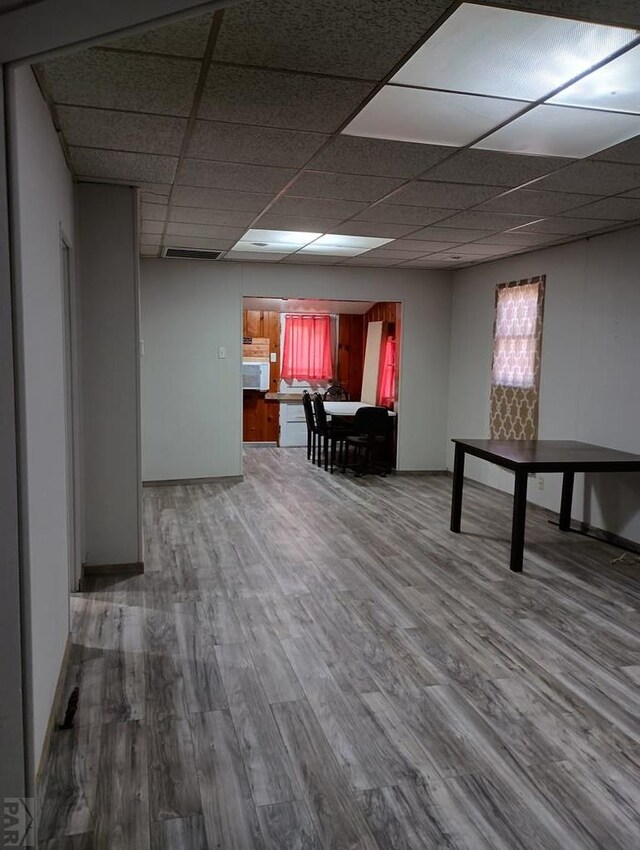 basement featuring a drop ceiling, wood finished floors, and baseboards