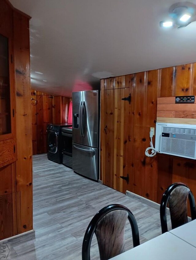 kitchen featuring brown cabinets, light wood-style floors, wooden walls, washer / dryer, and stainless steel fridge