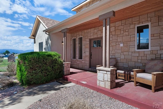 property entrance with stone siding, roof with shingles, and a patio area