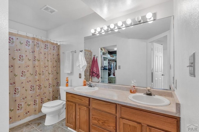 bathroom featuring a walk in closet, visible vents, a sink, and double vanity