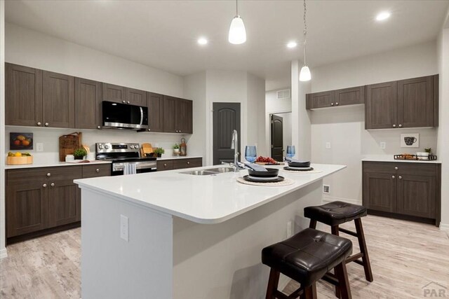 kitchen with a center island with sink, stainless steel appliances, light countertops, a sink, and a kitchen breakfast bar