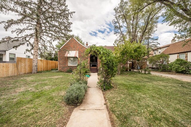 view of front of home featuring a front yard, brick siding, fence, and a chimney