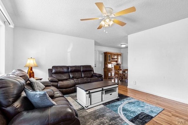 living area featuring a ceiling fan, a textured ceiling, baseboards, and wood finished floors