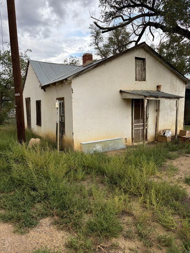 rear view of property with metal roof, a chimney, and stucco siding