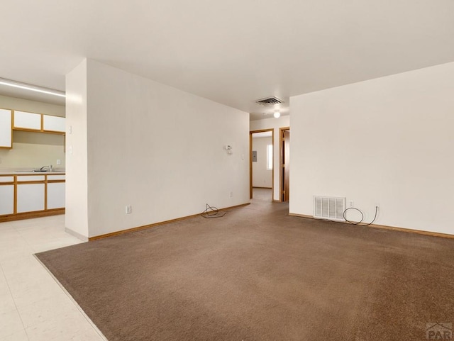 unfurnished living room with baseboards, visible vents, a sink, and light colored carpet