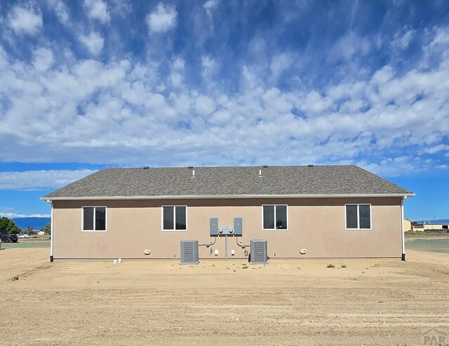 rear view of house with roof with shingles, central AC unit, and stucco siding