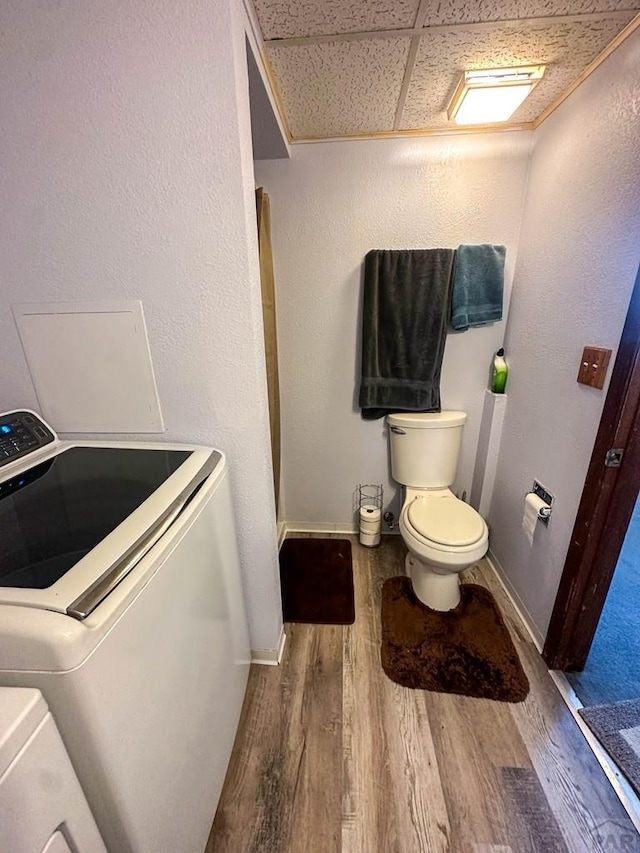 bathroom with a textured wall, wood finished floors, toilet, baseboards, and washing machine and clothes dryer
