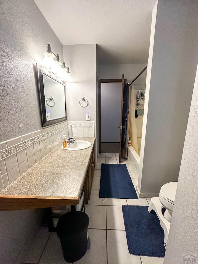 full bath featuring vanity, a textured wall, toilet, shower / bathtub combination with curtain, and tile patterned floors