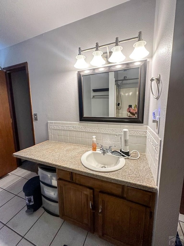 bathroom featuring vanity, decorative backsplash, a textured wall, walk in shower, and tile patterned floors