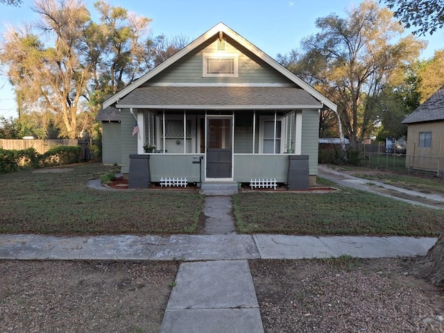 bungalow-style home with a shingled roof, a front yard, covered porch, and fence