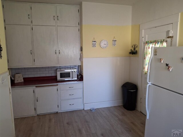 kitchen featuring white appliances, dark countertops, light wood-style flooring, and decorative backsplash