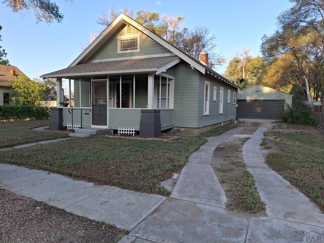 bungalow-style house with a garage, covered porch, a chimney, and a front lawn