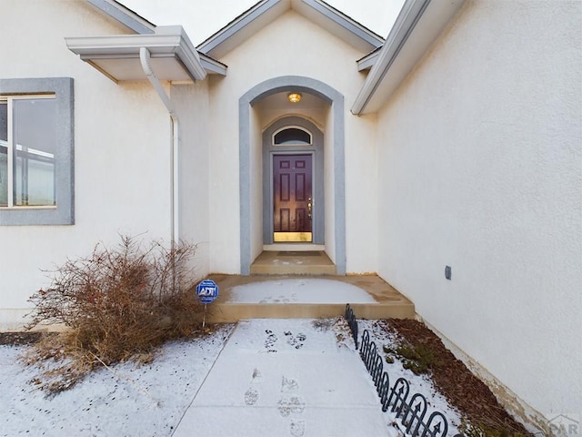 snow covered property entrance with stucco siding