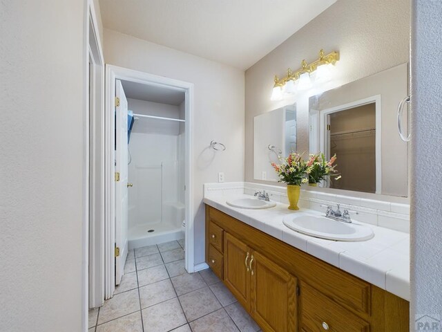 bathroom with a stall shower, double vanity, a sink, and tile patterned floors