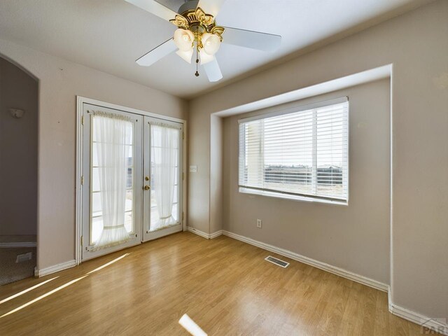 interior space with light wood finished floors, baseboards, visible vents, arched walkways, and french doors