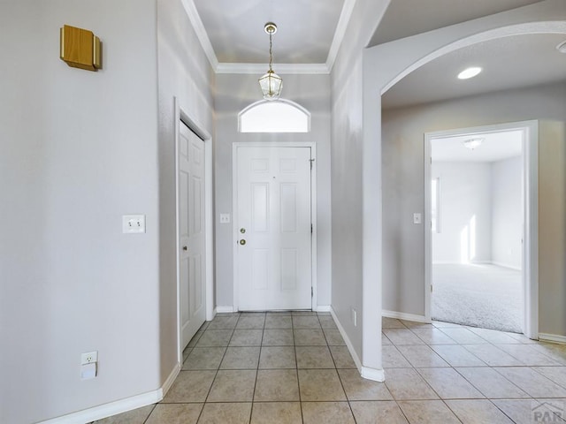 foyer entrance featuring light tile patterned floors, baseboards, arched walkways, and crown molding