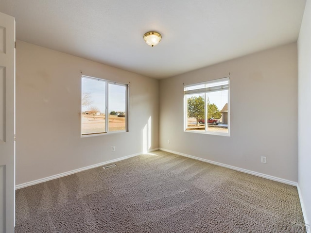 empty room with carpet, visible vents, and baseboards